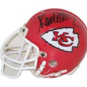 Könnte beinhalten: Ein roter Footballhelm mit einem weißen Gesichtsgitter und einem weißen Logo der Kansas City Chiefs. Der Helm ist mit "Kansas" in schwarzem Stift signiert.