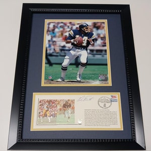 May include: A framed photograph of a football player wearing a blue and white uniform, holding a football. The photo is signed by the player and includes a smaller image of the player in a different uniform. The text below the photo reads "Professional Football Hall of Fame Induction".