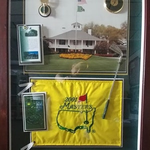 Puede incluir: Una impresión enmarcada de la casa club del Augusta National Golf Club con una bandera amarilla con el logotipo del Masters 2001 y un palo de golf verde.