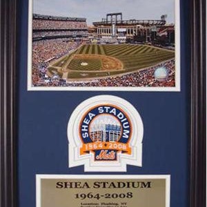 May include: A framed photo of Shea Stadium, home of the New York Mets from 1964 to 2008. The photo shows an aerial view of the stadium with fans in the stands. The frame includes a commemorative patch with the stadium's name and dates, and a plaque with details about the stadium.