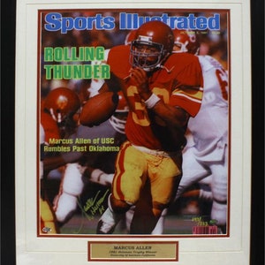 May include: Framed Sports Illustrated cover featuring Marcus Allen of USC in a football game. The cover has the headline "Rolling Thunder" and the date October 5, 1981. A gold plaque at the bottom reads "Marcus Allen 1981 Heisman Trophy Winner."