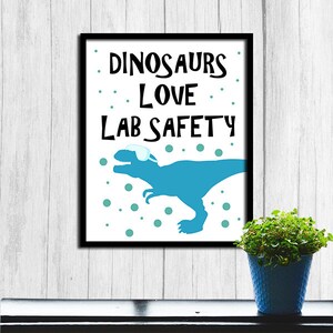 May include: A white framed poster with a blue dinosaur wearing safety goggles. The poster says "Dinosaurs Love Lab Safety".