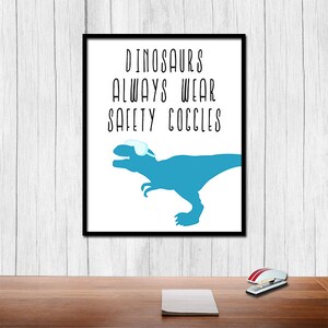 May include: A framed print with a blue dinosaur wearing safety goggles. The text on the print reads "Dinosaurs always wear safety goggles."