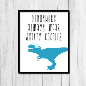 May include: A white framed print with a blue dinosaur wearing safety goggles. The text reads "Dinosaurs Always Wear Safety Goggles".