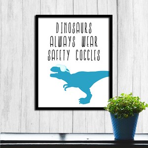 May include: A white framed print with a blue dinosaur wearing safety goggles. The text on the print reads "Dinosaurs always wear safety goggles."