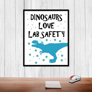 May include: A white poster with black text that reads "Dinosaurs Love Lab Safety". A blue dinosaur wearing safety goggles is shown in the poster. The background has teal dots.
