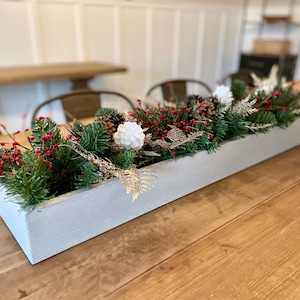 May include: A long, rectangular, gray concrete planter filled with a festive arrangement of pine branches, red berries, white pinecones, and silver fern sprigs.