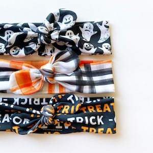 May include: Three black and white patterned headbands with orange and white plaid and black and white "trick or treat" text.