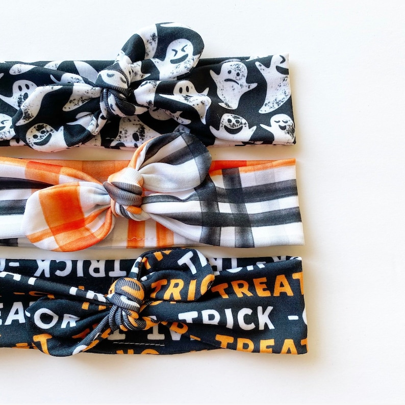May include: Three black and white patterned headbands with orange and white plaid and black and white "trick or treat" text.