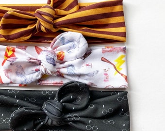 May include: Three headbands with different patterns. The top headband is brown and yellow striped. The middle headband is white with a pattern of magical objects. The bottom headband is black with a pattern of glasses.