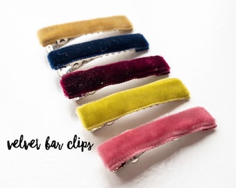 May include: Five velvet hair clips in different colors: mustard yellow, navy blue, burgundy, lime green, and dusty rose. The clips are arranged in a row, with the mustard yellow clip at the top and the dusty rose clip at the bottom.