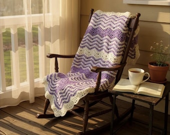 May include: A wooden rocking chair with a purple, cream, and white chevron-patterned blanket draped over it. A small side table holds a cup of tea and an open book. The scene is set on a wooden porch with sunlight streaming through a window.