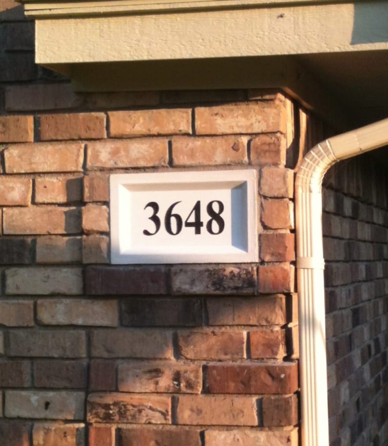 Puede incluir: Un letrero de n&uacute;mero de casa rectangular blanco con n&uacute;meros negros que dicen "3648" montado en una pared de ladrillo.
