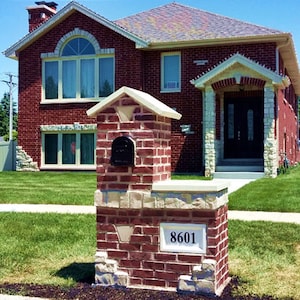 Puede incluir: Un buz&oacute;n de ladrillo con una puerta de buz&oacute;n negra y una placa blanca con el n&uacute;mero 8601. El buz&oacute;n est&aacute; delante de una casa de ladrillo rojo con un techo blanco.