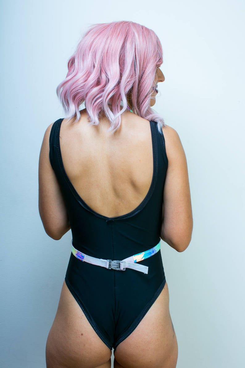 May include: A black swimsuit with a low back and a white iridescent belt. The model is wearing a pink wig.