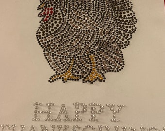 May include: A Thanksgiving-themed artwork featuring a turkey design made of brown, gold, and clear rhinestones. The turkey is set against a white background, with the words "HAPPY THANKSGIVING" spelled out in silver rhinestones below.