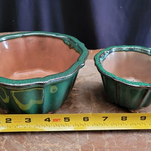 May include: Two green glazed ceramic pots with scalloped edges. The larger pot is 4 inches in diameter and the smaller pot is 3 inches in diameter.