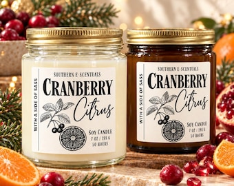 May include: Two glass jars of soy candle wax, one clear and one amber, each with a gold lid and a white label reading Southern E-Scentuals Cranberry Citrus with a side of sass, 7 oz / 198 g, 50 hours, featuring a botanical illustration.