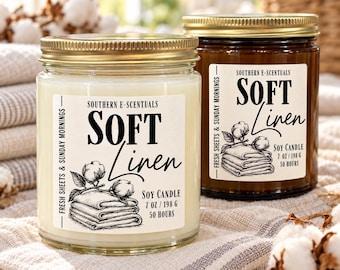 May include: Two glass jars of soy candle with gold lids. The labels read Southern E-Scentuals Soft Linen, Fresh Sheets & Sunday Mornings, 7 oz / 198 g, 50 hours. Each label features a black and white illustration of folded linens and cotton.