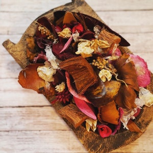 May include: A wooden tray filled with a colorful assortment of dried potpourri. The potpourri includes various textures and colors, such as brown, red, pink, and beige. The tray has a rustic, natural appearance, perfect for home decor.