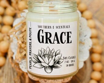 May include: A clear glass jar soy candle with a white label featuring the text Southern E-Scentuals, Grace, and Pearls, Prayers, & Polite. The label includes a black and white lotus flower illustration, 7 oz, 198 g, and 50 hours text.