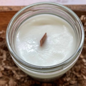 May include: A white candle in a clear glass jar with a wooden wick. The candle is almost completely full.