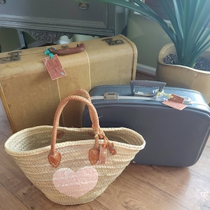 May include: Two vintage suitcases, one brown and one gray, with a straw tote bag with a pink heart design. The tote bag has leather handles and a tag with the word "Love" on it.