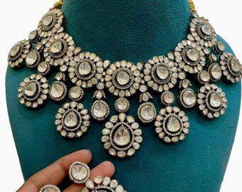 Puede incluir: Un conjunto de collar y pendientes de plata y blanco con piedras grandes, redondas y en forma de lágrima. El collar tiene un diseño en capas con varias filas de piedras y un diseño de lágrima colgante.