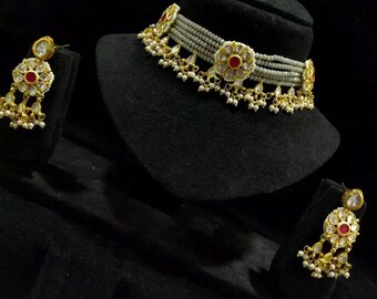 Puede incluir: Un collar gargantilla de oro con cuentas de perlas blancas y detalles de piedras preciosas rojas y transparentes. El collar tiene un diseño floral y viene con pendientes a juego.