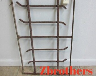 May include: A rusty metal window grate with five horizontal bars. The grate is attached to a white wall. A small white tag with the number "326" written on it is attached to the top of the grate.