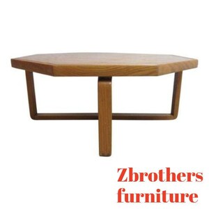 May include: A hexagonal wooden coffee table with a simple, mid-century modern design. The table has a light brown wood finish and a geometric base.
