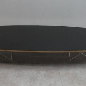 May include: An oval-shaped coffee table with a dark gray top and a light wood edge. The table is supported by a silver metal base with a geometric design. The table is approximately 60 inches long.