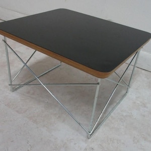 May include: A small, rectangular coffee table with a black top and a natural wood edge. The table has a chrome-colored, geometric wireframe base. The table is approximately 18 inches long, 12 inches wide, and 16 inches tall.