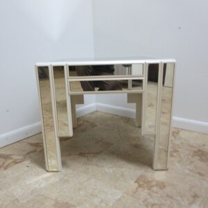 May include: A white mirrored end table with a geometric design. The table has a square top and four legs.