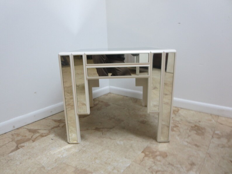 May include: A white mirrored end table with a geometric design. The table has a square top and four legs.