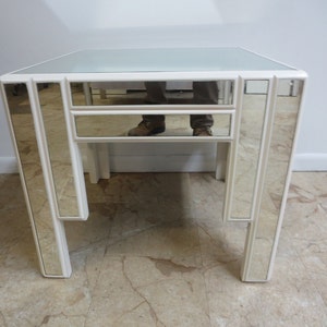 May include: A white mirrored end table with a geometric design. The table has a glass top and a single drawer.