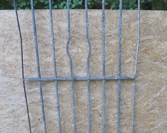 May include: A metal gate with a simple design, featuring vertical bars and curved accents. The gate is made of a dark gray metal and is set against a brown wooden background.