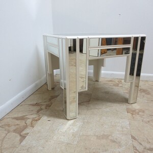 May include: A white mirrored side table with a square top and four legs. The table has a geometric design with mirrored panels.