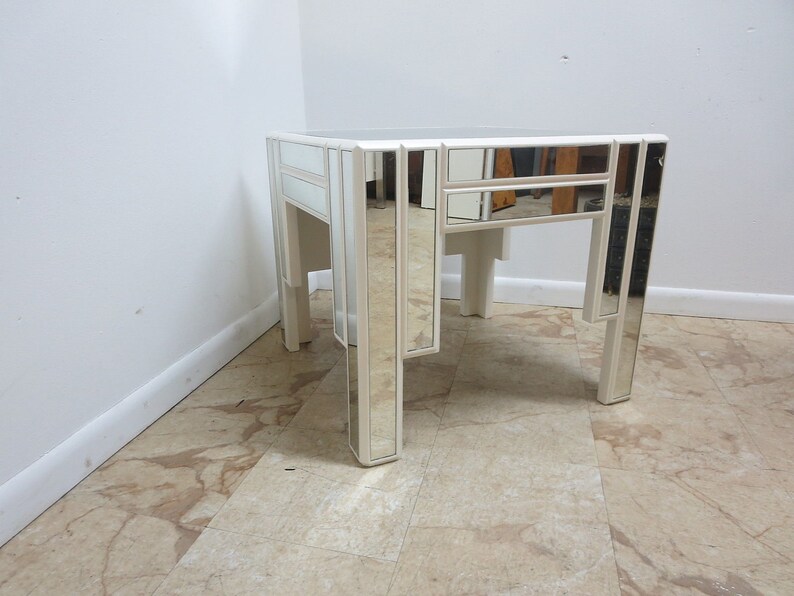 May include: A white mirrored side table with a square top and four legs. The table has a geometric design with mirrored panels.