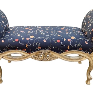 May include: A decorative chaise lounge with a dark blue floral patterned seat and backrests. The frame is a light gold color with ornate carvings and curved legs. The overall design is elegant and vintage.