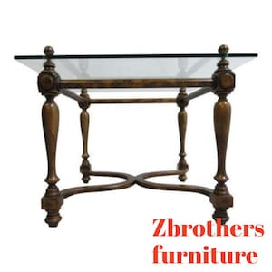 May include: A square glass-top coffee table with a wooden frame. The table has four legs with ornate details and a decorative cross-shaped base.