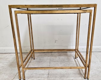 May include: A gold metal nesting table set with two glass shelves. The table is made of a thin metal frame and has a simple, modern design.