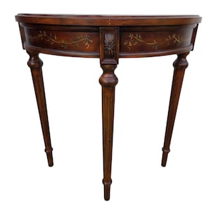 May include: A half-moon shaped wooden console table with three slender legs. The dark brown table features floral painted accents and a carved central support. The table's top is approximately 30 inches wide.