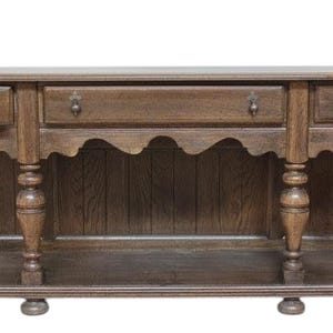 May include: A dark brown wooden sideboard with three drawers and decorative pulls. The sideboard has a scalloped apron and turned legs. A lower shelf runs the length of the piece. The wood grain is visible.