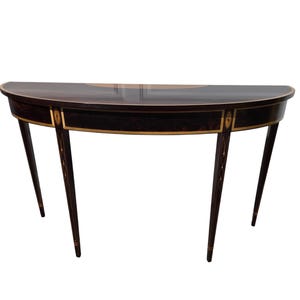 May include: A half-moon shaped, dark wood console table with gold trim. The table has four slender, tapered legs and a decorative gold inlay on the tabletop. The table's design is classic and elegant, suitable for a hallway or living room.