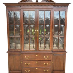 May include: A large, dark brown wooden cabinet with glass-paned doors and drawers. The cabinet has a decorative top and brass hardware. The glass doors reflect the surrounding environment. The cabinet is a classic piece of furniture.