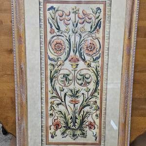 May include: A framed print of a vintage floral design with intricate details in shades of green, orange, and brown. The design features stylized flowers and leaves, creating a symmetrical pattern.
