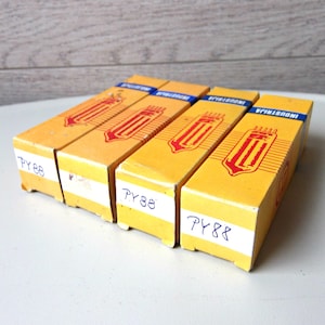 Puede incluir: Cuatro cajas amarillas vintage con detalles rojos y azules. Cada caja presenta un gráfico rojo y la palabra "INDUSTRIA" en azul. Las cajas tienen etiquetas blancas con el texto manuscrito "PY88".