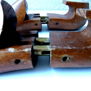 K&ouml;nnte beinhalten: Nahaufnahme von zwei Schuhspannern aus Holz. Die Spanner sind mittelbraun mit Messingbeschl&auml;gen. Die Holzteile haben eine gebogene Form, die f&uuml;r den Einsatz in einem Schuh konzipiert ist. Die Spanner sind auf einer wei&szlig;en Oberfl&auml;che positioniert.