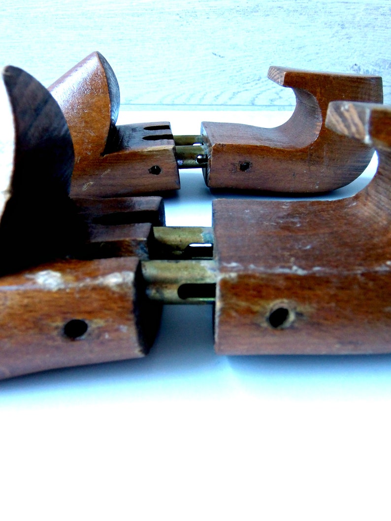 K&ouml;nnte beinhalten: Nahaufnahme von zwei Schuhspannern aus Holz. Die Spanner sind mittelbraun mit Messingbeschl&auml;gen. Die Holzteile haben eine gebogene Form, die f&uuml;r den Einsatz in einem Schuh konzipiert ist. Die Spanner sind auf einer wei&szlig;en Oberfl&auml;che positioniert.